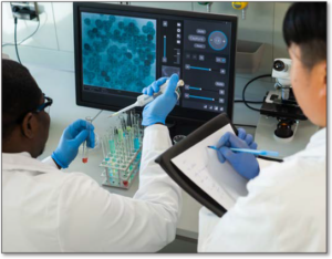Photo of two lab technicians. One person is writing on a piece of paper while the other is using a pipette and looking at the computer screen.