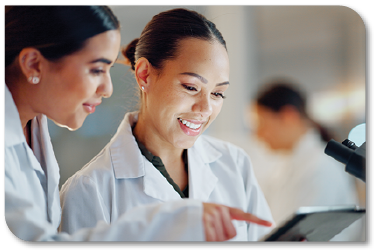 Two women in lab coats conversing over a computer